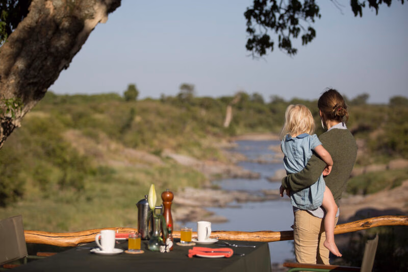 A woman and child look out at a river from a breakfast table during a luxury Kenya family safari.