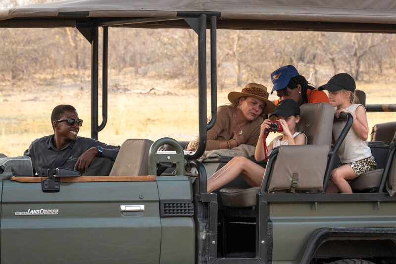 A woman and children in a safari vehicle looking at a camera held by a young girl.