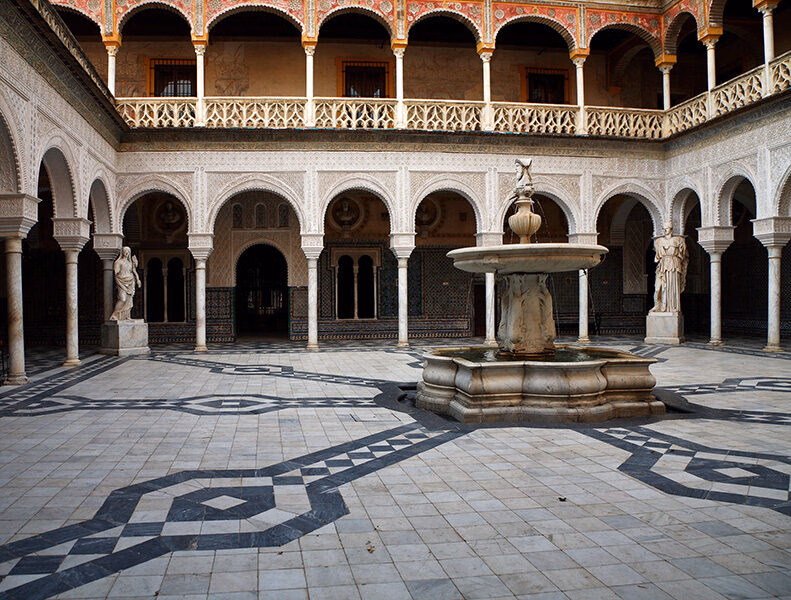 Ornate, arcaded Mudejar-style courtyard with tiled floor and central fountain. Perfect setting for luxury Spain holidays.