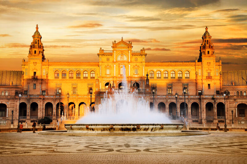Plaza de España building in Seville glowing at sunset with a fountain in the center, ideal for luxury Spain vacations.
