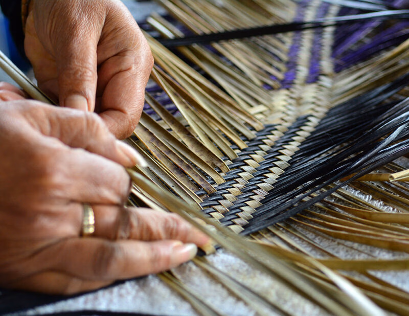 Hands performing traditional flax weaving with purple and natural fibers during luxury New Zealand holidays.