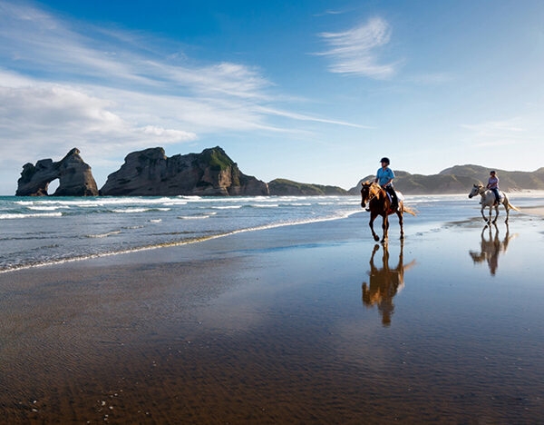 Jacada New Zealand - person on horseback rides along a beach at low tide