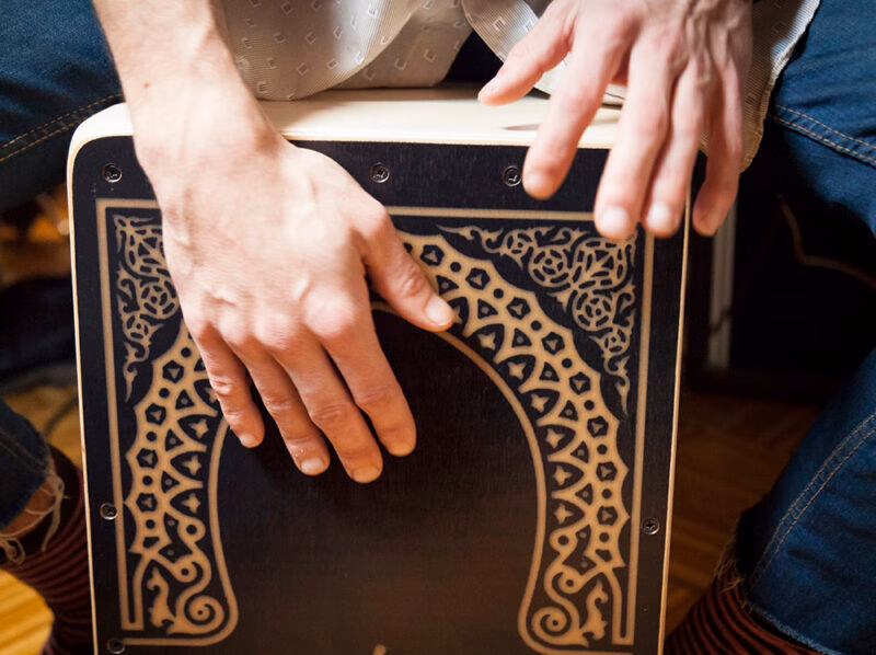 Close-up of a person's hands playing the top of a decorated wooden cajon drum, a sound of luxury Portugal vacations.