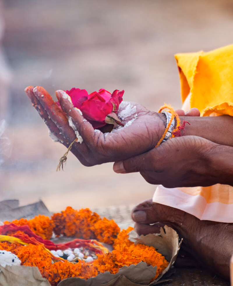 Hands holding a red flower and white powder over orange marigold garlands during a traditional Hindu ritual on luxury India tours.