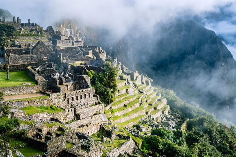 The ruins of Machu Picchu are dramatically visible on a steep, misty mountainside, featuring stone structures and terraces, ideal for luxury Machu Picchu trips.