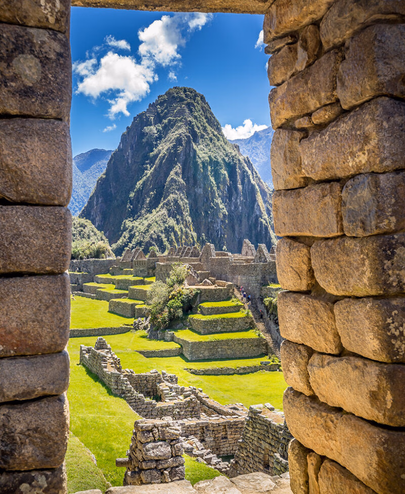 A view of Machu Picchu ruins, green grass, and Huayna Picchu mountain, framed by two weathered stone walls, suggesting luxury Machu Picchu vacations.
