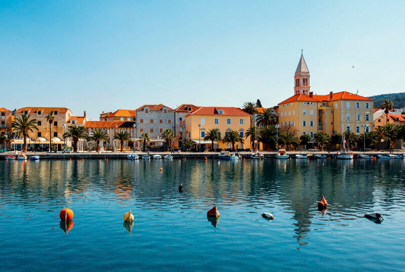 Waterfront buildings and palm trees reflected in a calm harbor during luxury Croatia trips.