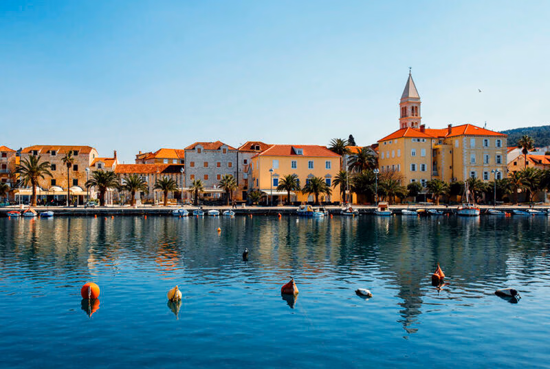 Waterfront buildings and palm trees reflected in a calm harbor during luxury Croatia trips.