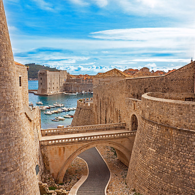 Medieval stone bridge and defensive walls of an old city harbor during luxury Croatia holidays.