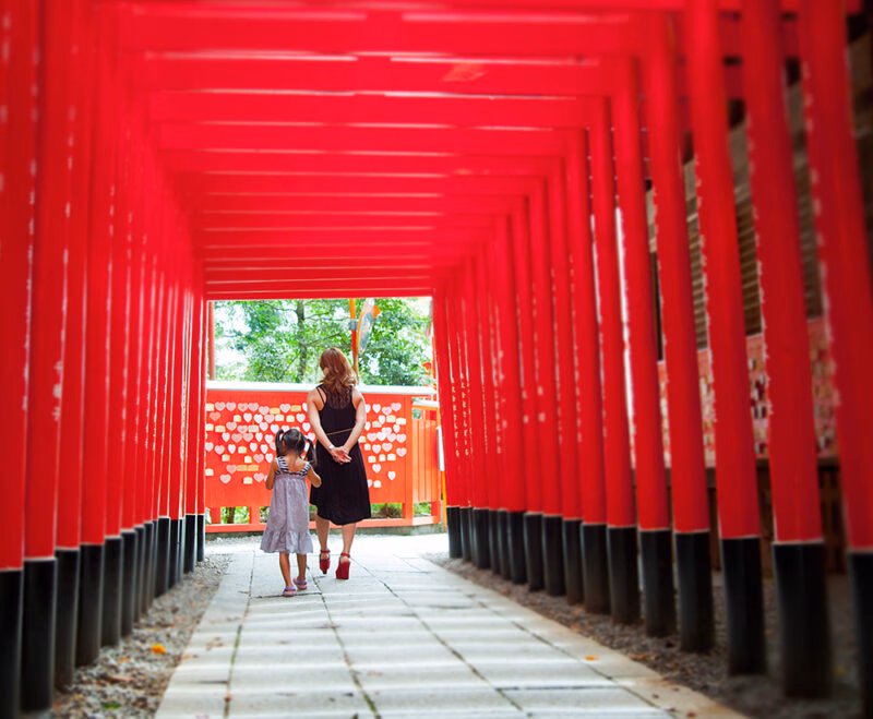 A woman and child walk through a tunnel of vibrant red torii gates while enjoying luxury family holidays to Japan.