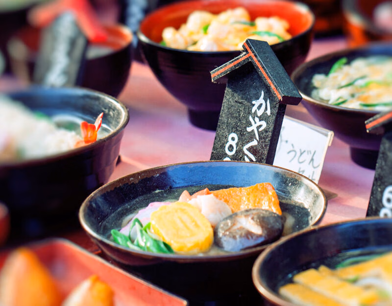 A vibrant display of plastic food models featuring udon bowls with mushrooms and egg, perfect for luxury family tours to Japan.