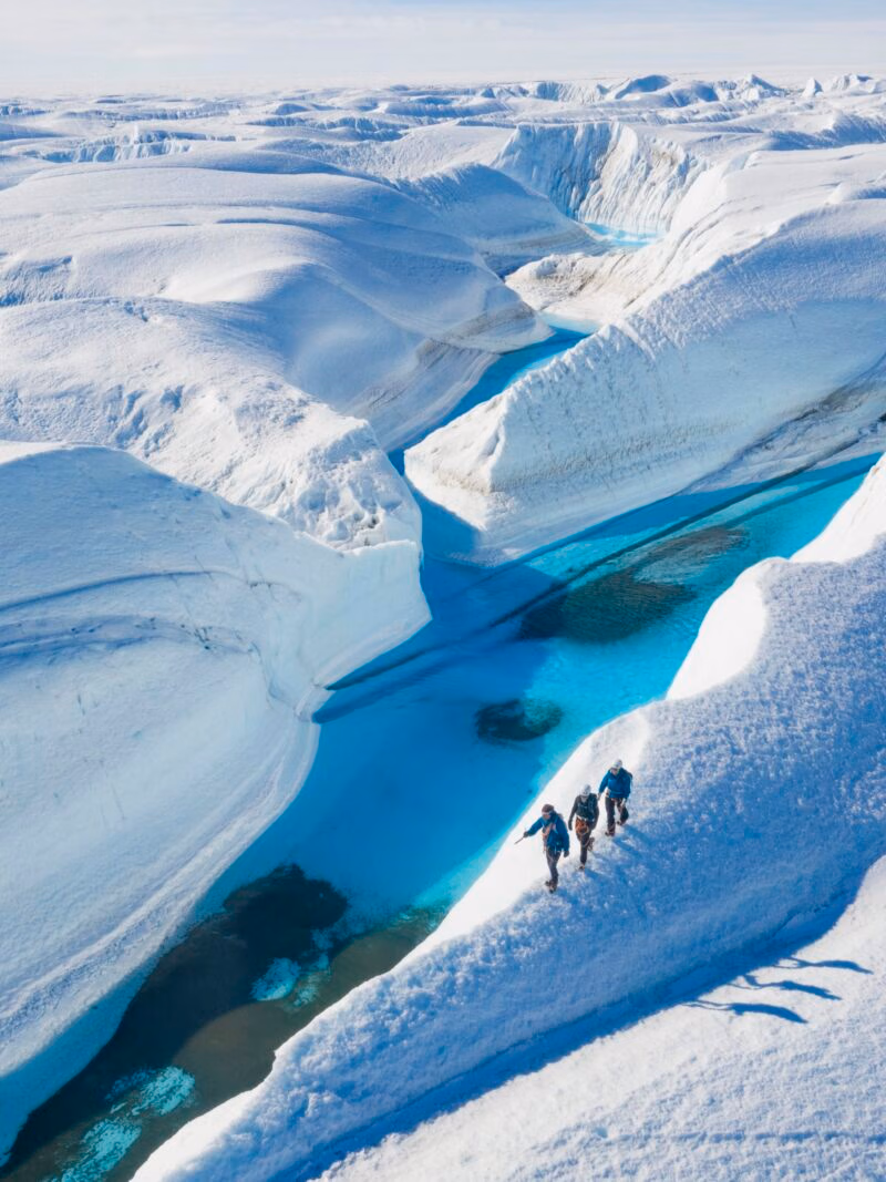 Aerial view of hikers on snow ridges by turquoise water, featured on luxury Polar trips.