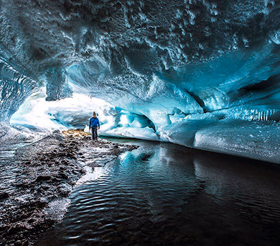 A person exploring a large ice cave with frozen ripples, part of Luxury Polar tours.