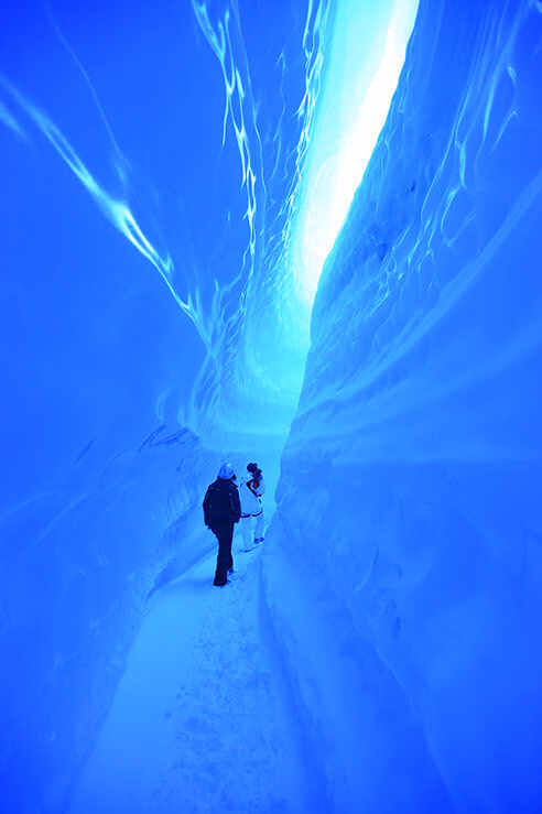 Two people walking through a vibrant blue ice cave, an activity offered on luxury Polar vacations.