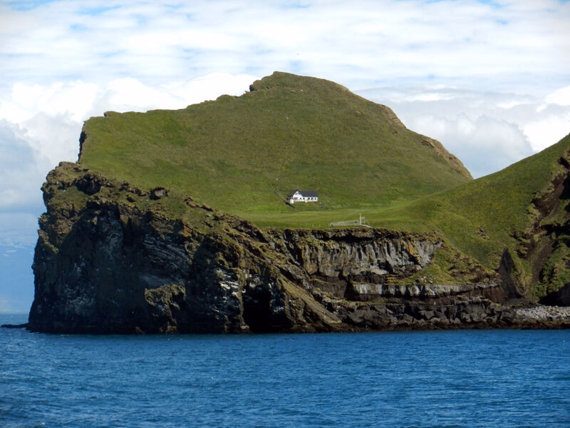 A white house on a green cliff surrounded by blue water, visited during luxury Polar holidays.