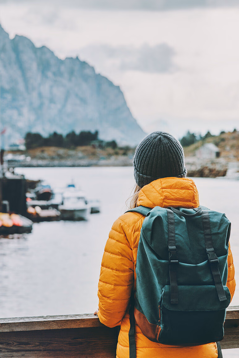 A hiker in an orange jacket viewing an Arctic harbor, a scene from luxury Polar vacations.