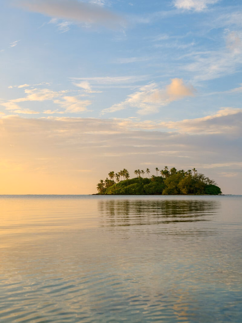 A remote tropical island surrounded by calm water at sunset on luxury Australasia tours.