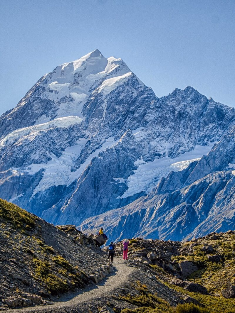 Hikers on a trail below a majestic snow-capped mountain peak on luxury Australasia holidays.