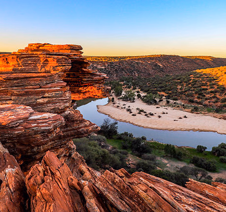 Dramatic red rock canyon cliffs overlooking a serene river during luxury Australasia vacations.