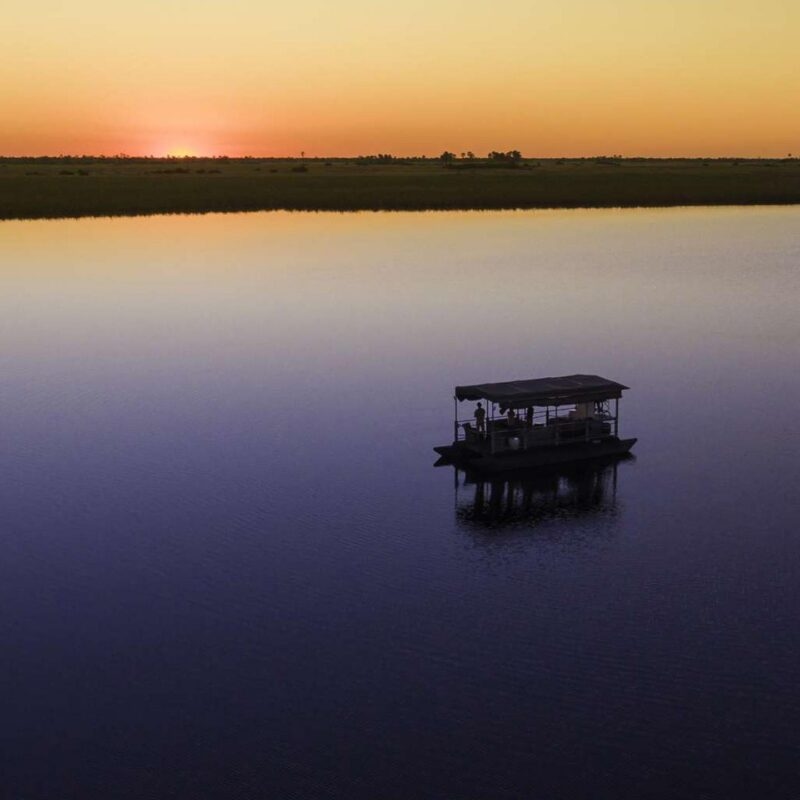 Aerial view of a boat on a vast river at sunset with an orange sky reflecting on the water.