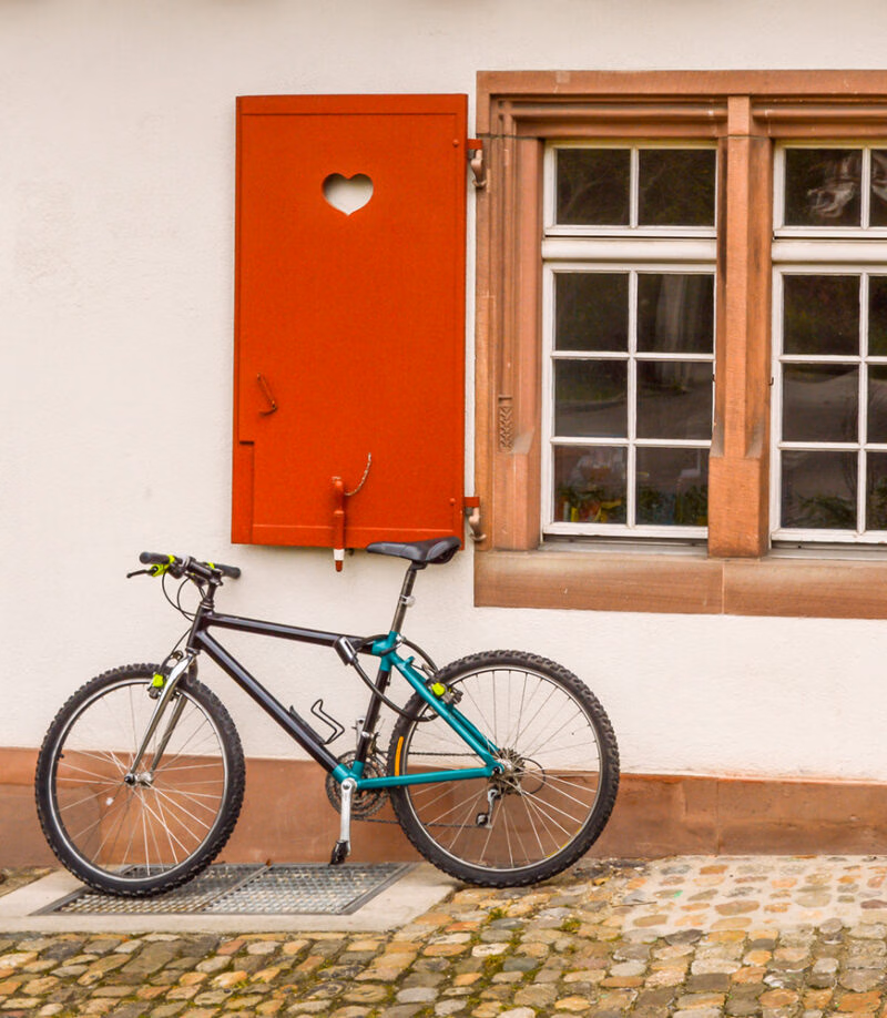 Bicycle parked against a building with a red wooden window shutter featuring a heart cutout on luxury Switzerland tours.