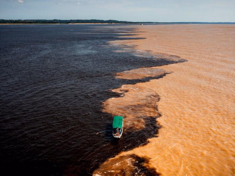 Aerial view of the "Meeting of Waters," where two rivers of distinct colors converge, with a boat in the center. luxury Brazil vacations.