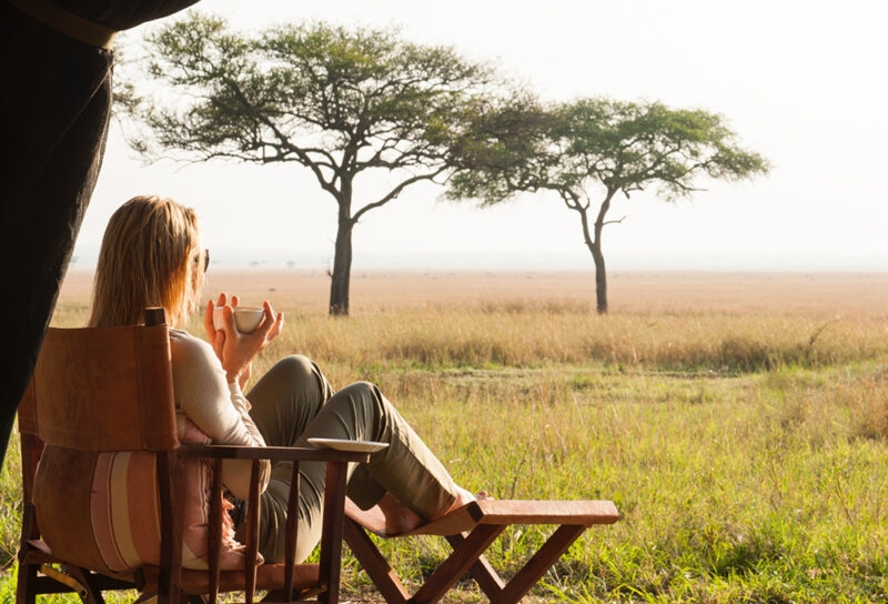 A woman sitting in a chair drinking coffee looking out over African landscape