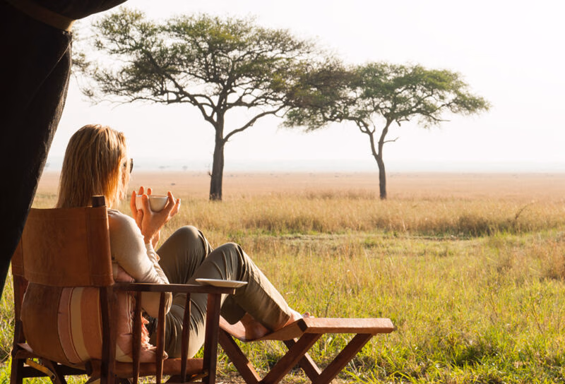A woman sitting in a wooden chair watching the sunset during luxury Serengeti National Park tours.
