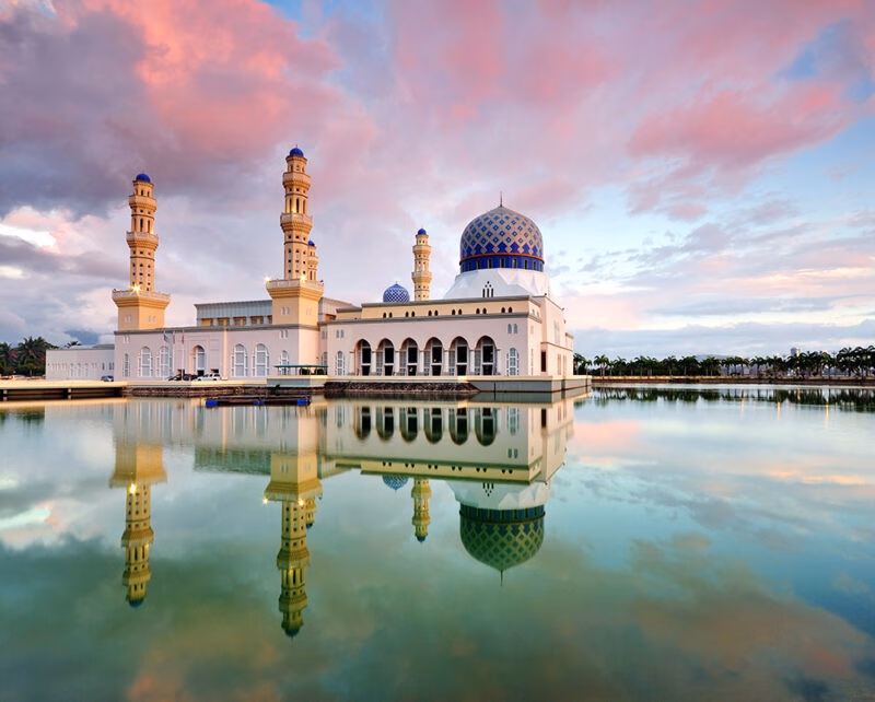 A beautiful white mosque with blue domes reflected in calm water during luxury Borneo holidays.