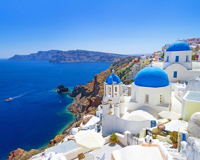 The bright white buildings and famous blue-domed churches of Santorini, Greece, overlooking the deep blue Aegean Sea and volcanic caldera.