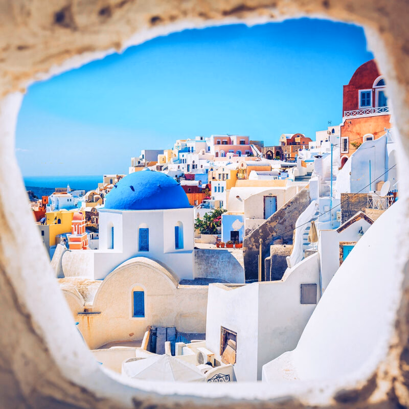 The bright white buildings and famous blue-domed churches of Santorini, Greece, overlooking the deep blue Aegean Sea and volcanic caldera.
