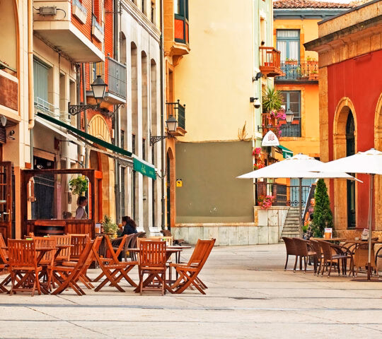 Empty cafe tables on a sunlit street with colorful buildings during luxury Portugal holidays.