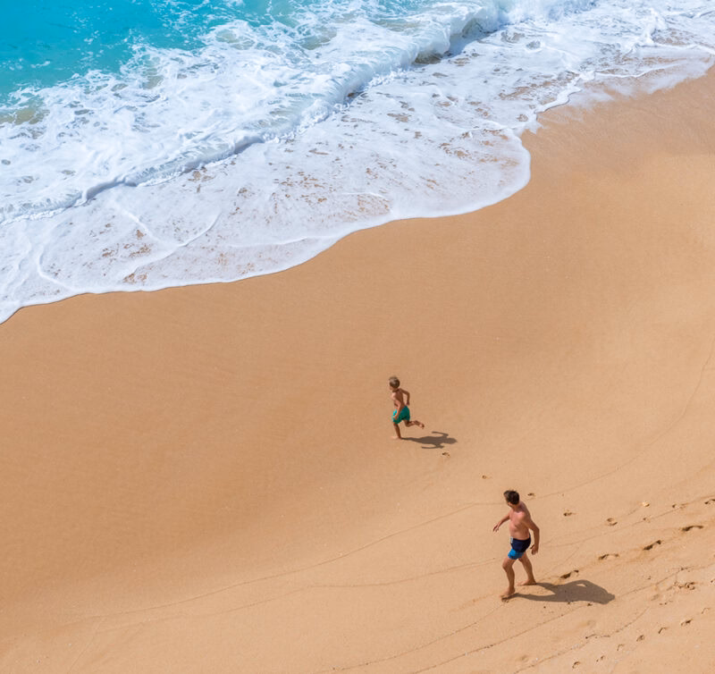 A father and his child running along a golden sand beach, Carvalho of Algarve, Portugal