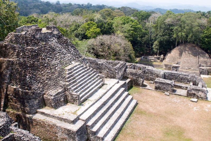 Ancient stone pyramid ruins and courtyards nestled within a thick green tropical forest.