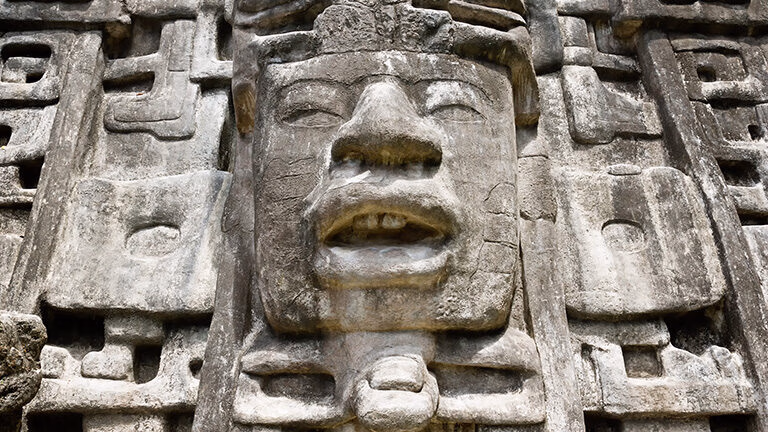 Close-up of an ancient stone face carving with detailed features on a weathered wall.