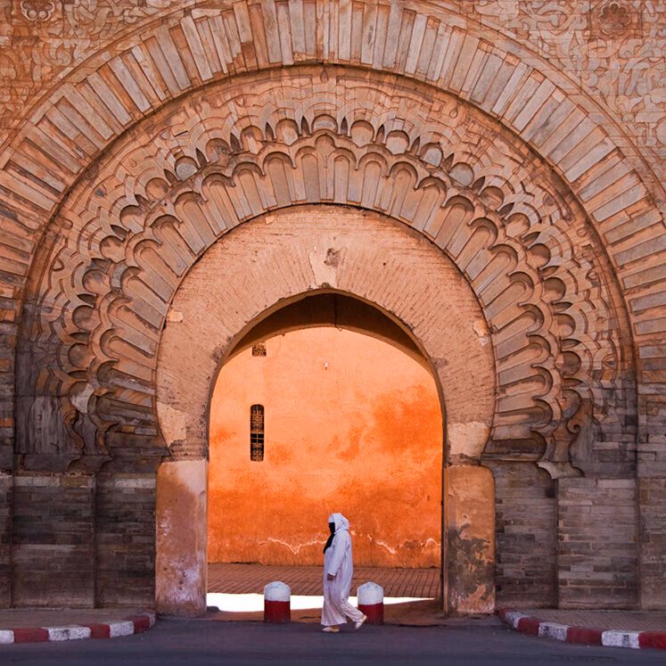 A person in white traditional clothing walks through a massive stone arch on luxury Africa honeymoon vacations.
