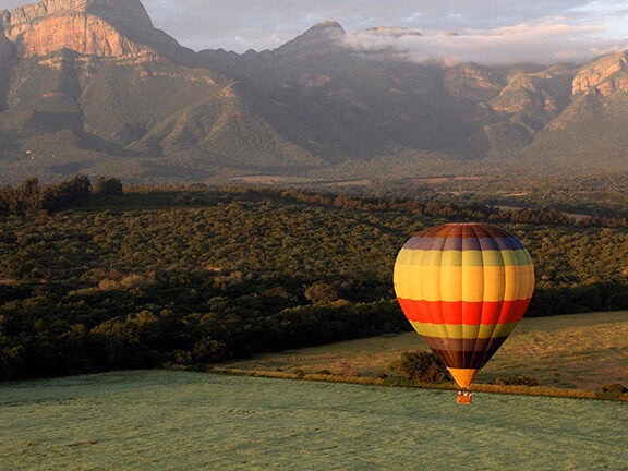 A yellow, red, and green hot air balloon gliding over a valley for luxury Africa honeymoon tours.