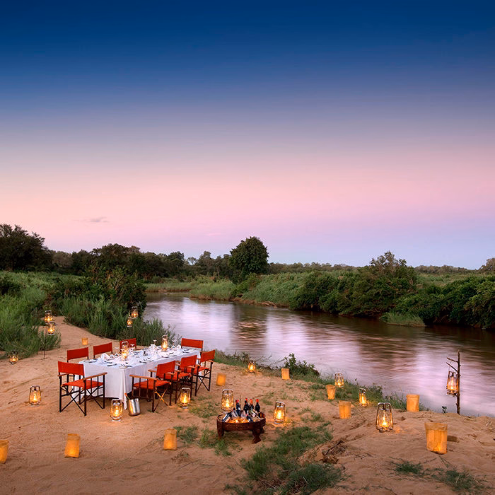 A romantic dinner table with red chairs by a river during luxury Africa honeymoon trips.