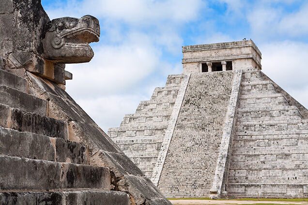 The El Castillo pyramid at Chichen Itza with a Mayan serpent head carving in the foreground, for luxury Latin America grand tour vacations.