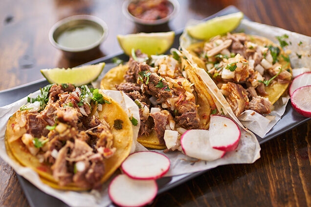 Platter of three authentic Mexican tacos topped with meat and garnishes, served with lime and radishes, luxury Latin America grand tours.
