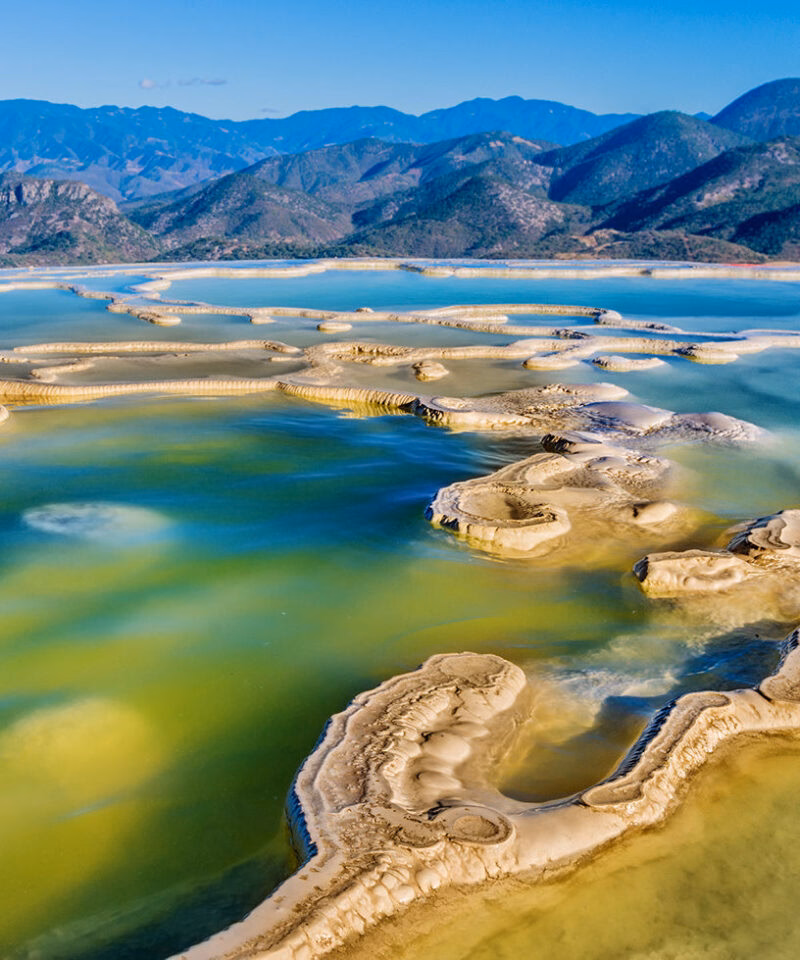 Striking travertine rock terraces and pools of Hierve el Agua with aqua and green water, backed by distant mountains, luxury Latin America grand tour holidays.