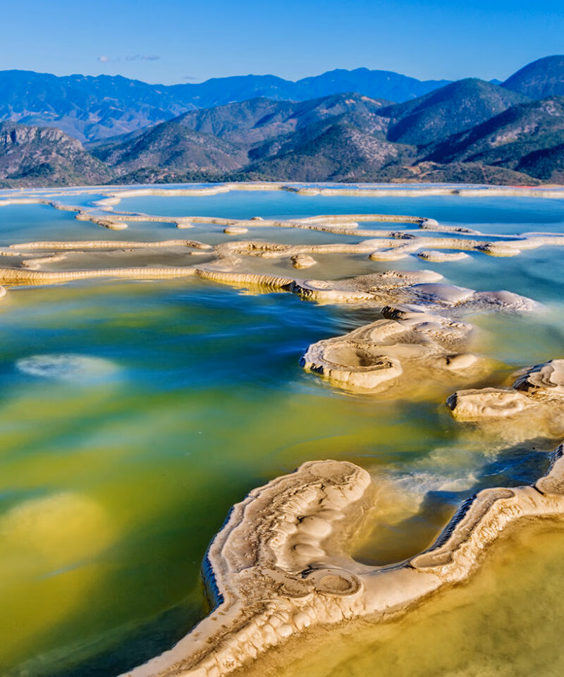 Striking travertine rock terraces and pools of Hierve el Agua with aqua and green water, backed by distant mountains, luxury Latin America grand tour holidays.