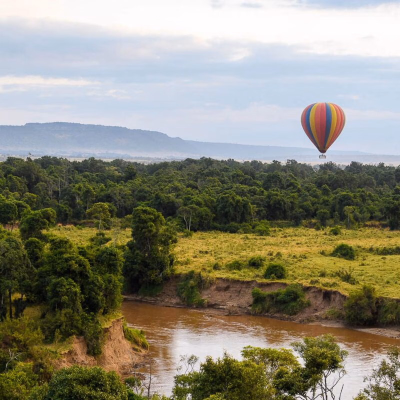 A hot air balloon drifting over a scenic river bend during luxury Maasai Mara holidays.