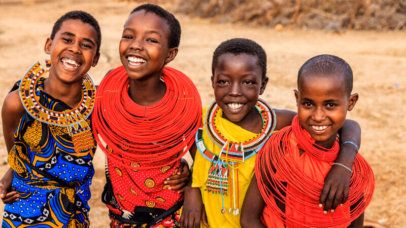 Smiling children wearing intricate traditional beaded necklaces during luxury Maasai Mara holidays.