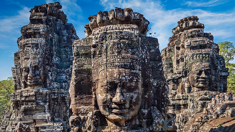 Close-up of three ancient, weathered stone temple towers from Bayon, Angkor Thom, each featuring a colossal, carved, smiling face.