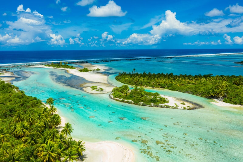Aerial view of lush green tropical islands and clear blue water channels on luxury French Polynesia trips.