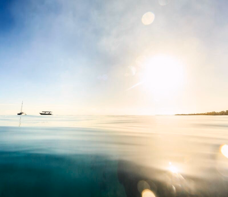 Bright sun reflecting on calm sea water with boats on the horizon during luxury French Polynesia holidays.