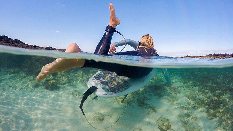 Split level view of a person on a surfboard over a clear sandy seabed on luxury French Polynesia tours.