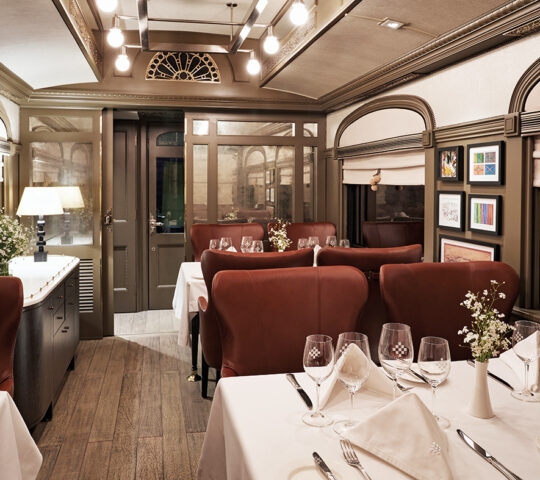 Interior of a luxury train dining car with set tables, leather chairs, and warm ambient lighting.