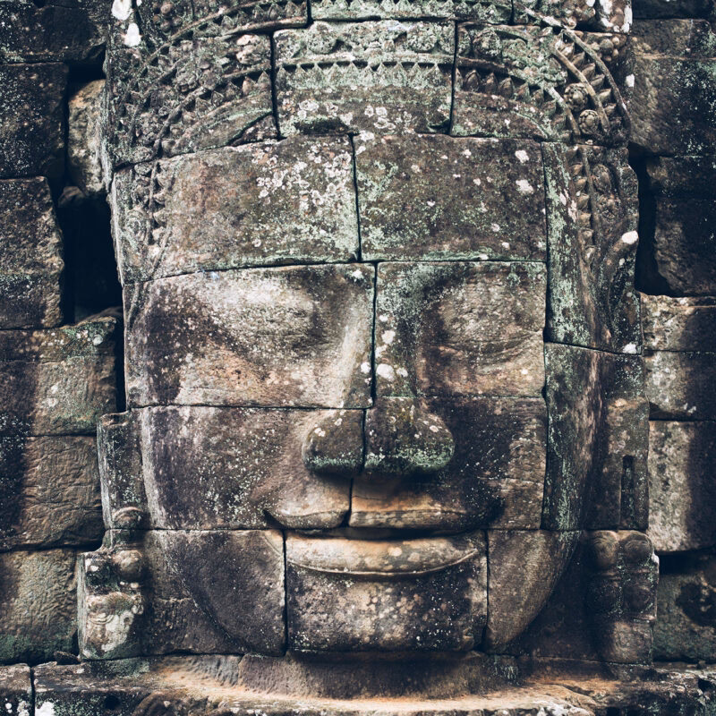 Ancient serene stone face carving at a temple site during luxury grand tours.